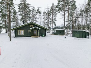 A cabin with a front porch and a garage, surrounded by snow-covered trees.