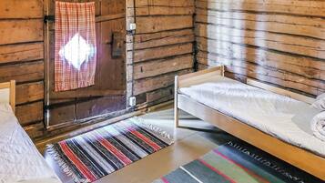 A cabin interior with a bed, a window with a plaid curtain, and a wooden wall.
