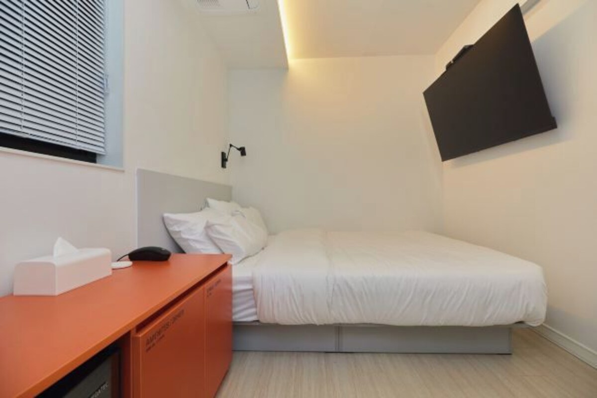 Une chambre d’hôtel moderne équipée d’un lit, d’un bureau avec un téléphone et d’un téléviseur fixé au mur.