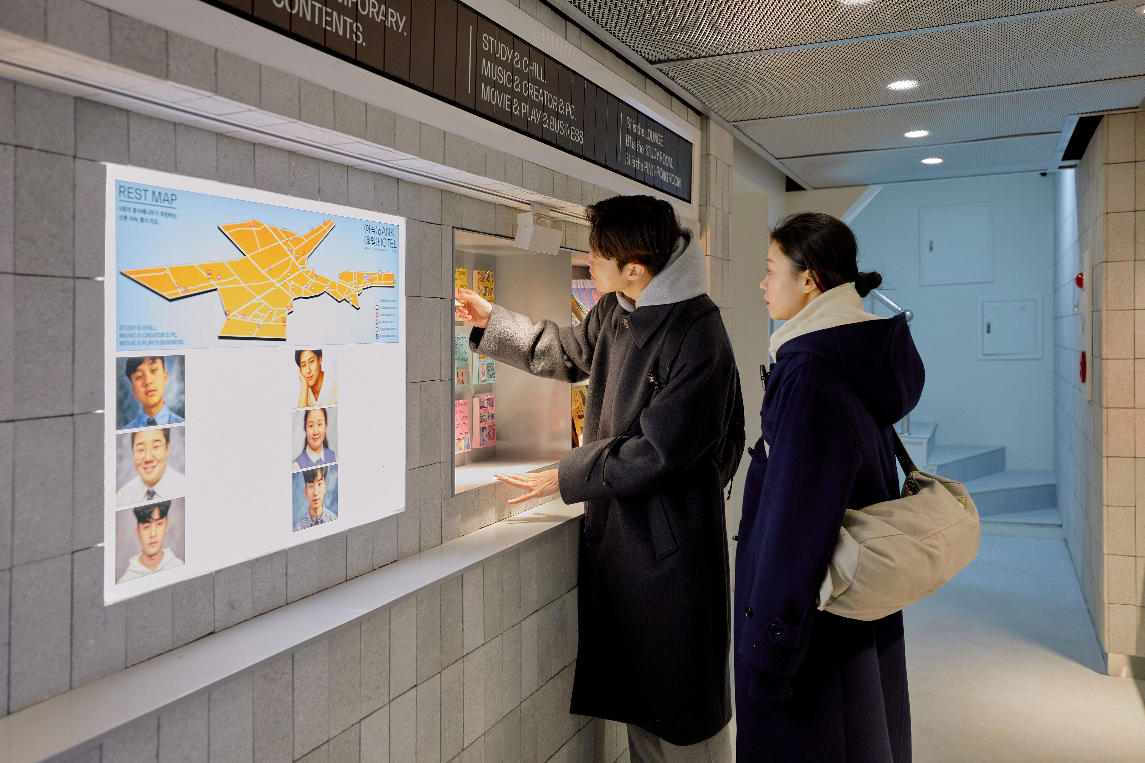 Un homme et une femme sont en train de regarder un mur où sont accrochés une carte et des photos.