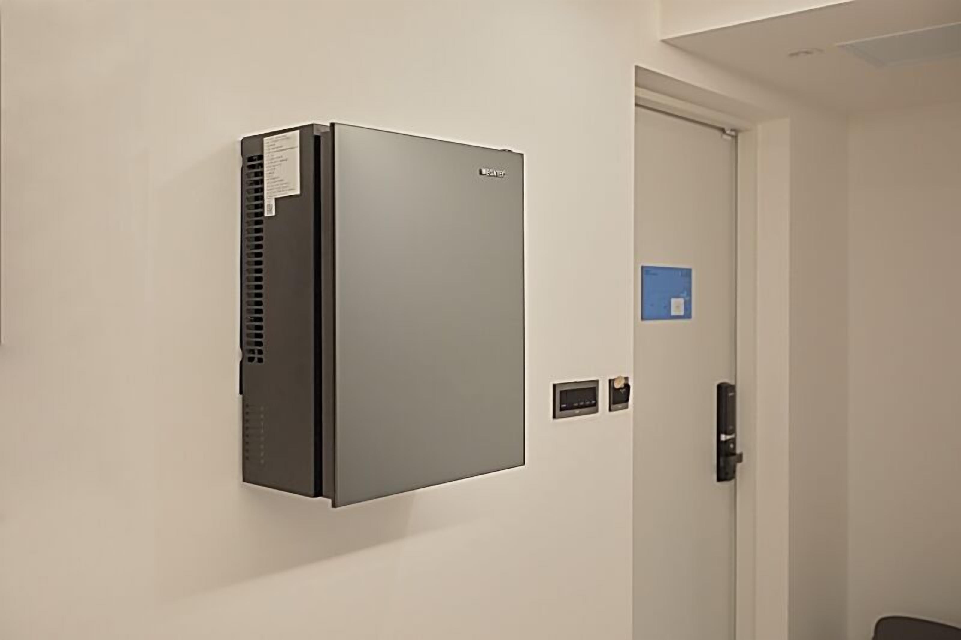 Un climatiseur mural moderne, installé dans une pièce avec une porte blanche et un petit panneau bleu sur le mur.