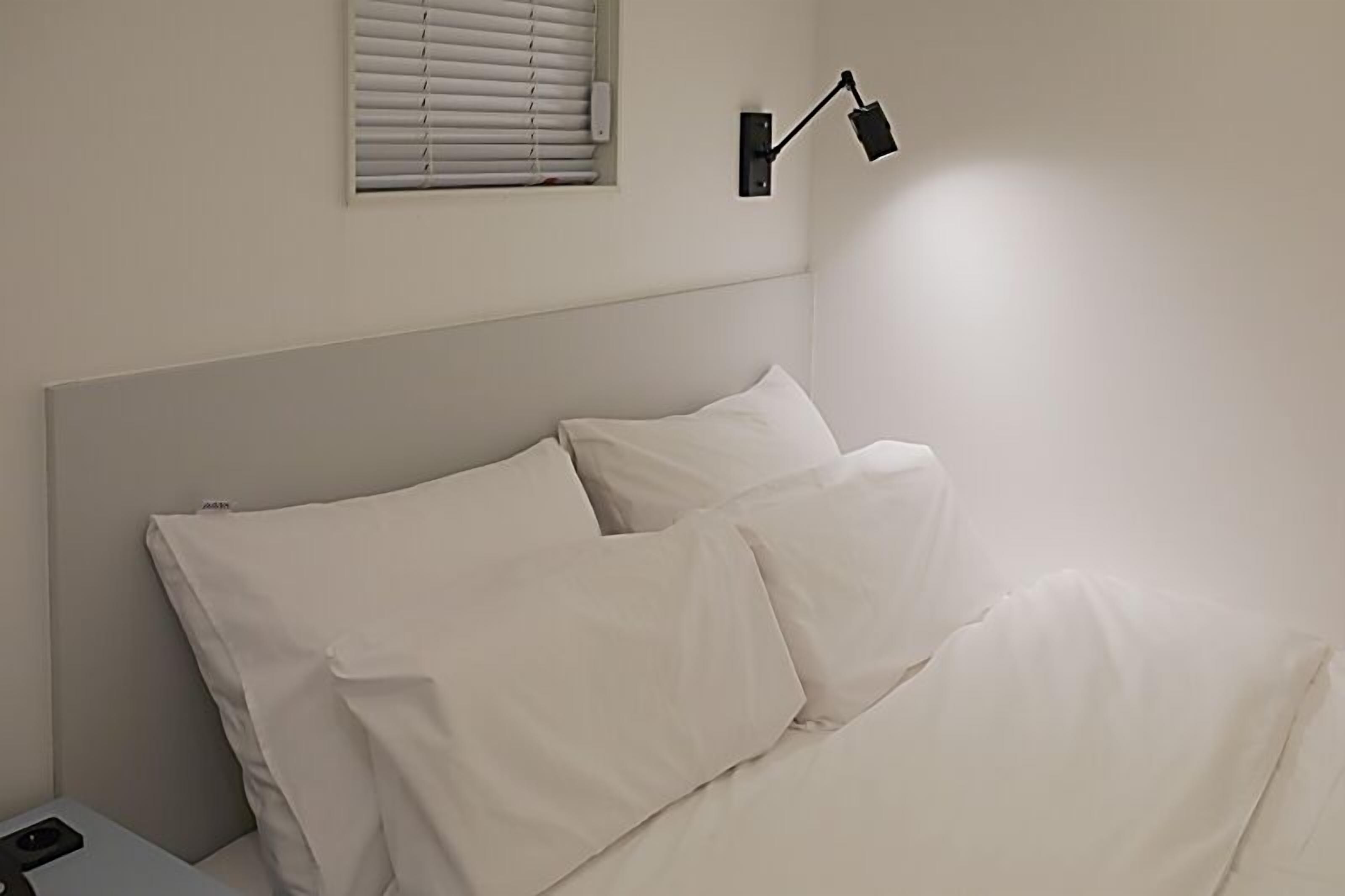 A neatly made bed with white linens and a single bedside lamp.