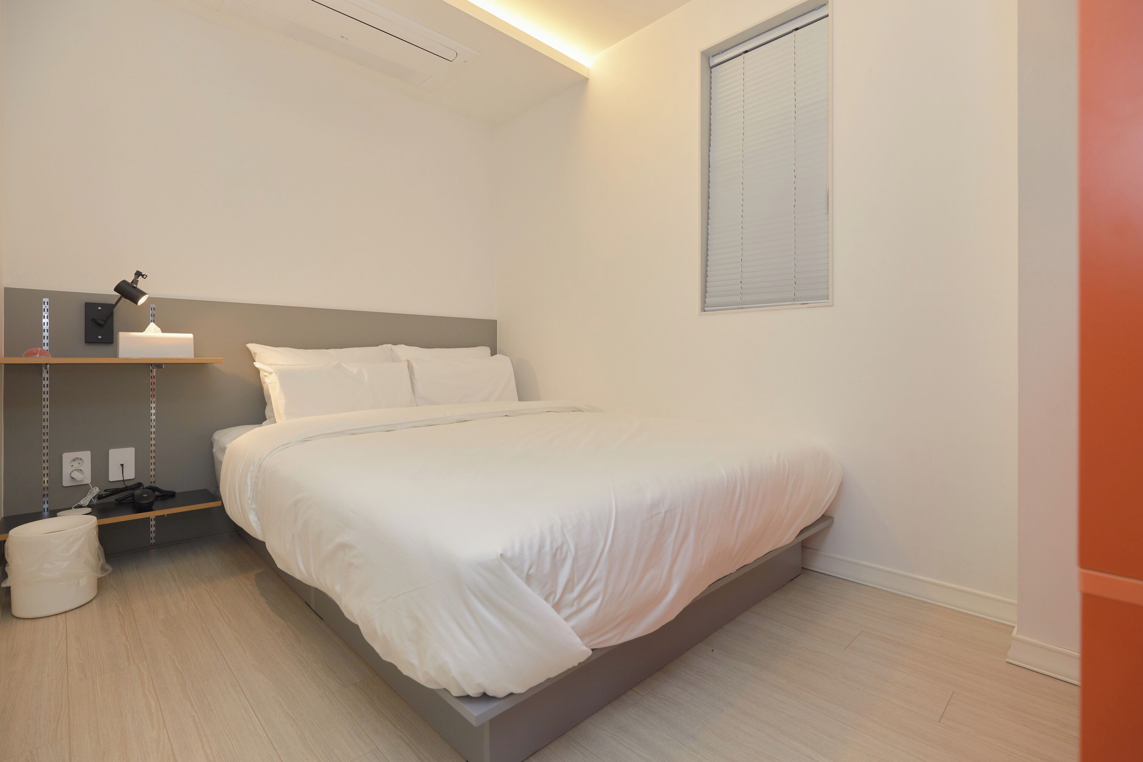 Un dormitorio moderno con cama, mesita de noche, lámpara y ventana con persianas.