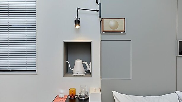 Una camera d'albergo moderna con un letto, un comodino con una lampada, una macchina per il caffè e un quadro appeso al muro.