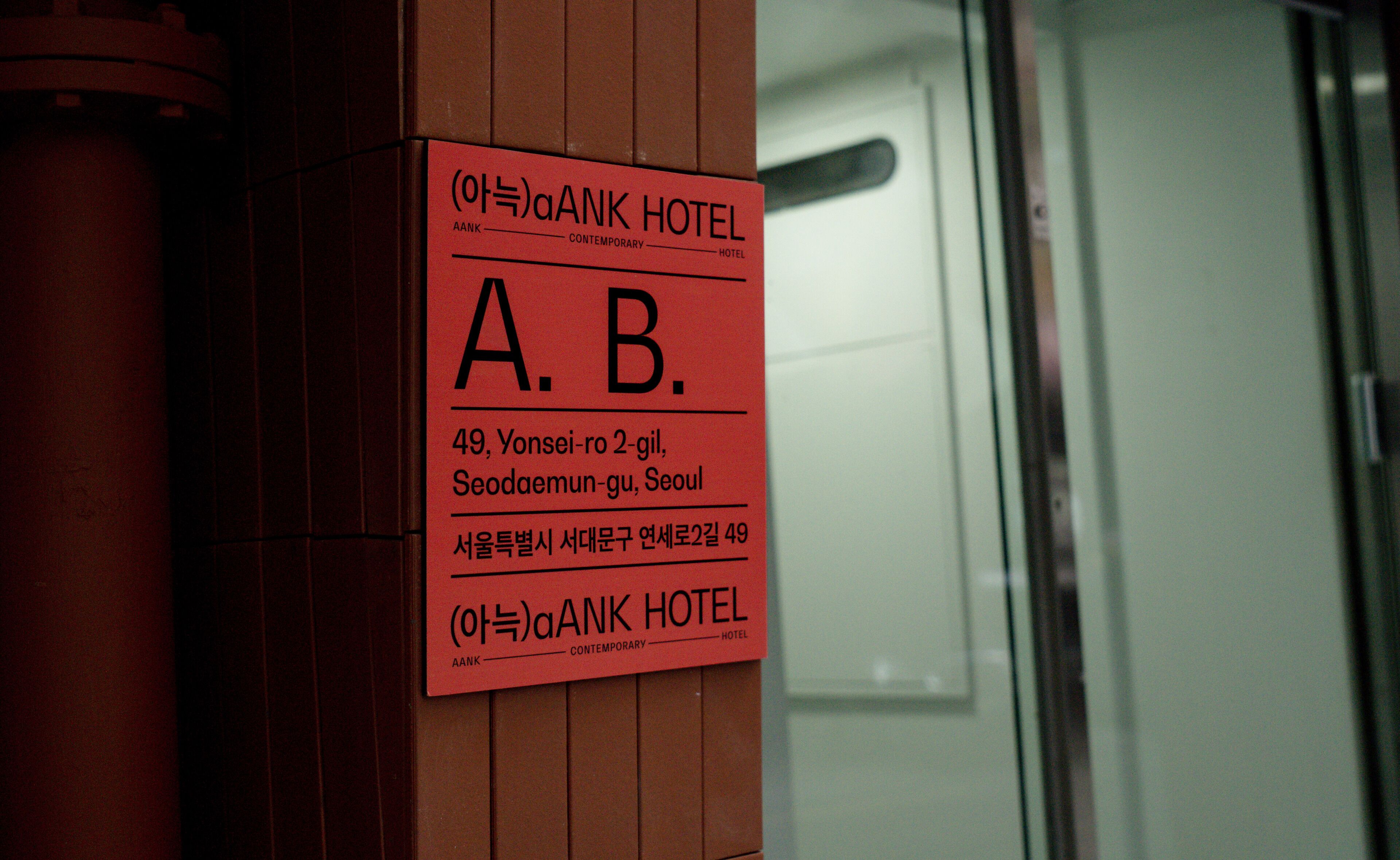 Uma placa vermelha com o nome 'A. B.' e endereço do Hotel AANK em Seul.