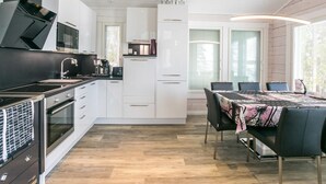 Een moderne keuken met witte kasten, een zwarte kookplaat en een eethoek met een tafel en stoelen.