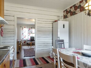 A kitchen with a stove, sink, and refrigerator. There is a dining table with chairs and a rug.