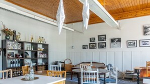A cozy dining area with wooden tables and chairs, a bookshelf with various items, and framed pictures on the wall.