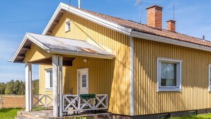 A yellow wooden house with a porch, a chimney, and a small garden area.