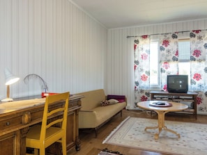 A room with a wooden desk, a chair, a sofa, a television on a stand, and a patterned curtain.