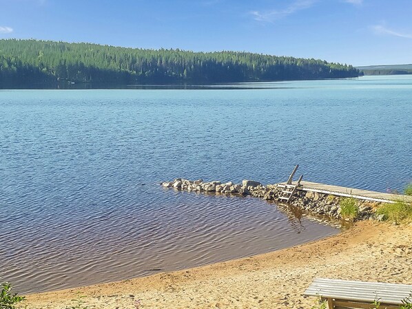 A calm lake with a wooden dock extending into the water, surrounded by a forested shoreline.