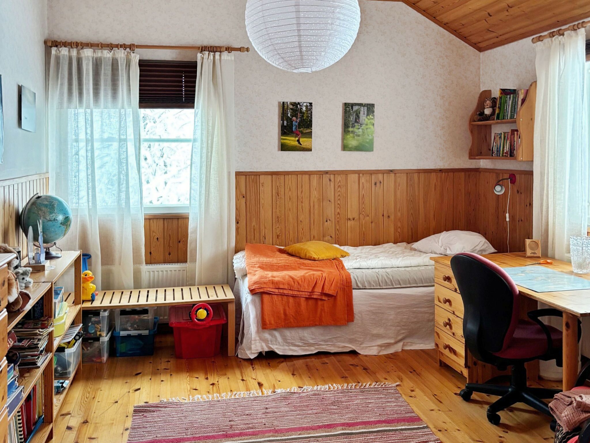 A cozy bedroom with a wooden bunk bed, a desk with a chair, a globe, and bookshelves.