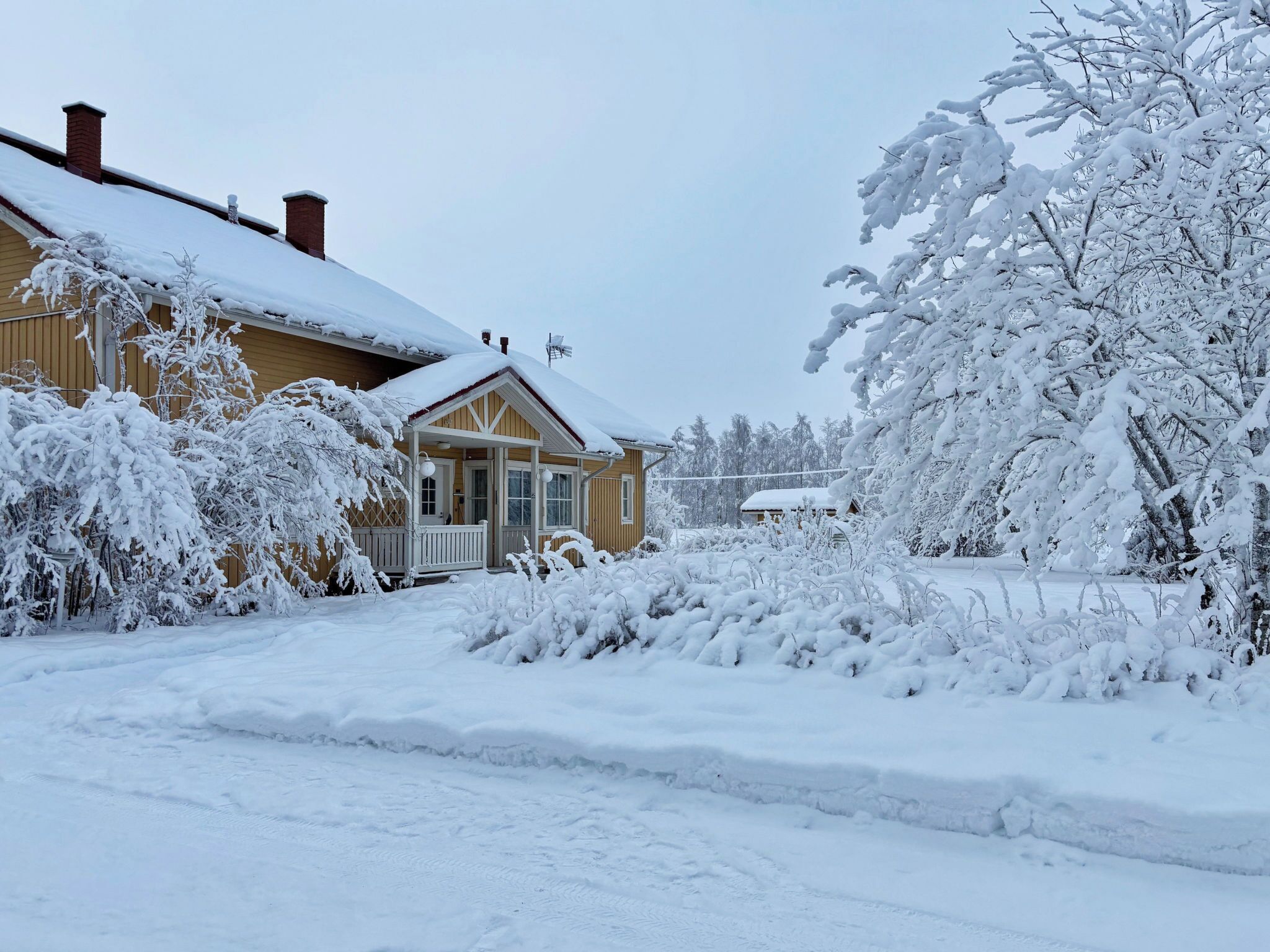 Et hus dækket af sne med veranda og skorsten.