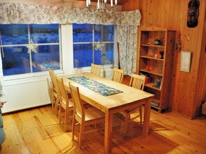 Un comedor de madera con una mesa y sillas, una ventana con cortinas y una estantería con diversos objetos.