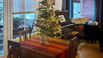 Un salón acogedor con un árbol de Navidad, un piano y un comedor con una mesa dispuesta para dos.
