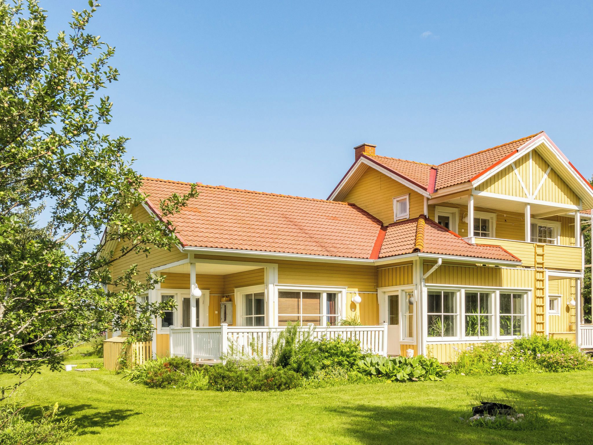 Une maison à deux étages, avec un toit recouvert de tuiles rouges, un balcon et une pelouse bien entretenue.