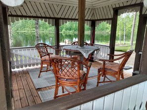 A covered outdoor seating area with a table and chairs, overlooking a lake. - Kaislaranta by Interhome (Suonenjoki)