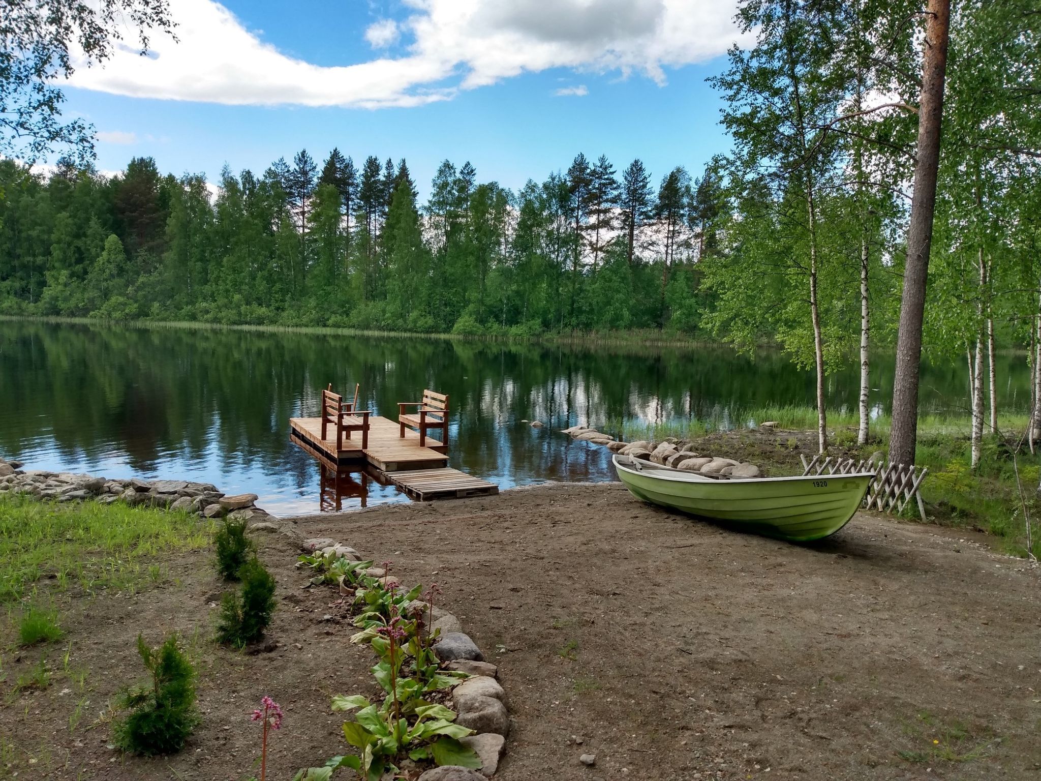 Un refugio junto al lago con un muelle, sillas de madera y un bote.