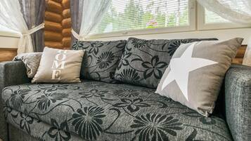 Un sofá gris con tapicería floral y dos almohadones, uno con el texto 'HOME', en una habitación con ventana y cortinas.