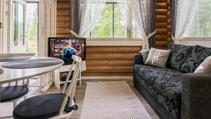 A cozy log cabin interior with a dining area, a sofa, and a television displaying a show. - Kaislaranta by Interhome (Suonenjoki)