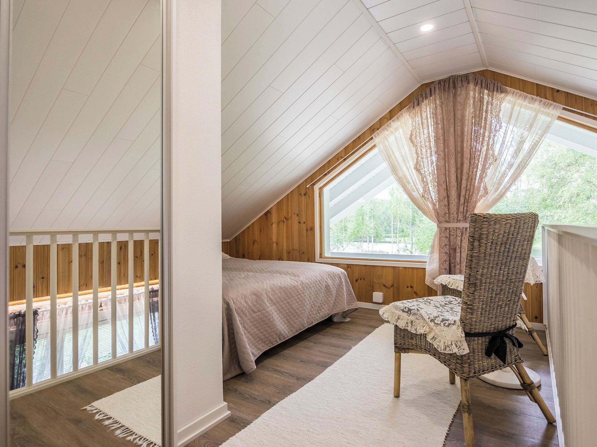 A bedroom with a sloped ceiling, a bed, a chair, and a window with curtains.