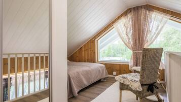 A bedroom with a sloped ceiling, a bed, a chair, and a window with curtains.