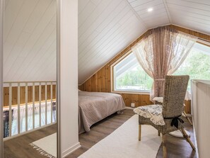 A bedroom with a sloped ceiling, a bed, a chair, and a window with curtains. - Kaislaranta by Interhome (Suonenjoki)