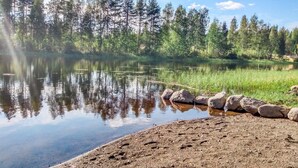 A calm lake with a sandy shore, surrounded by dense trees and a clear sky. - Kaislaranta by Interhome (Suonenjoki)