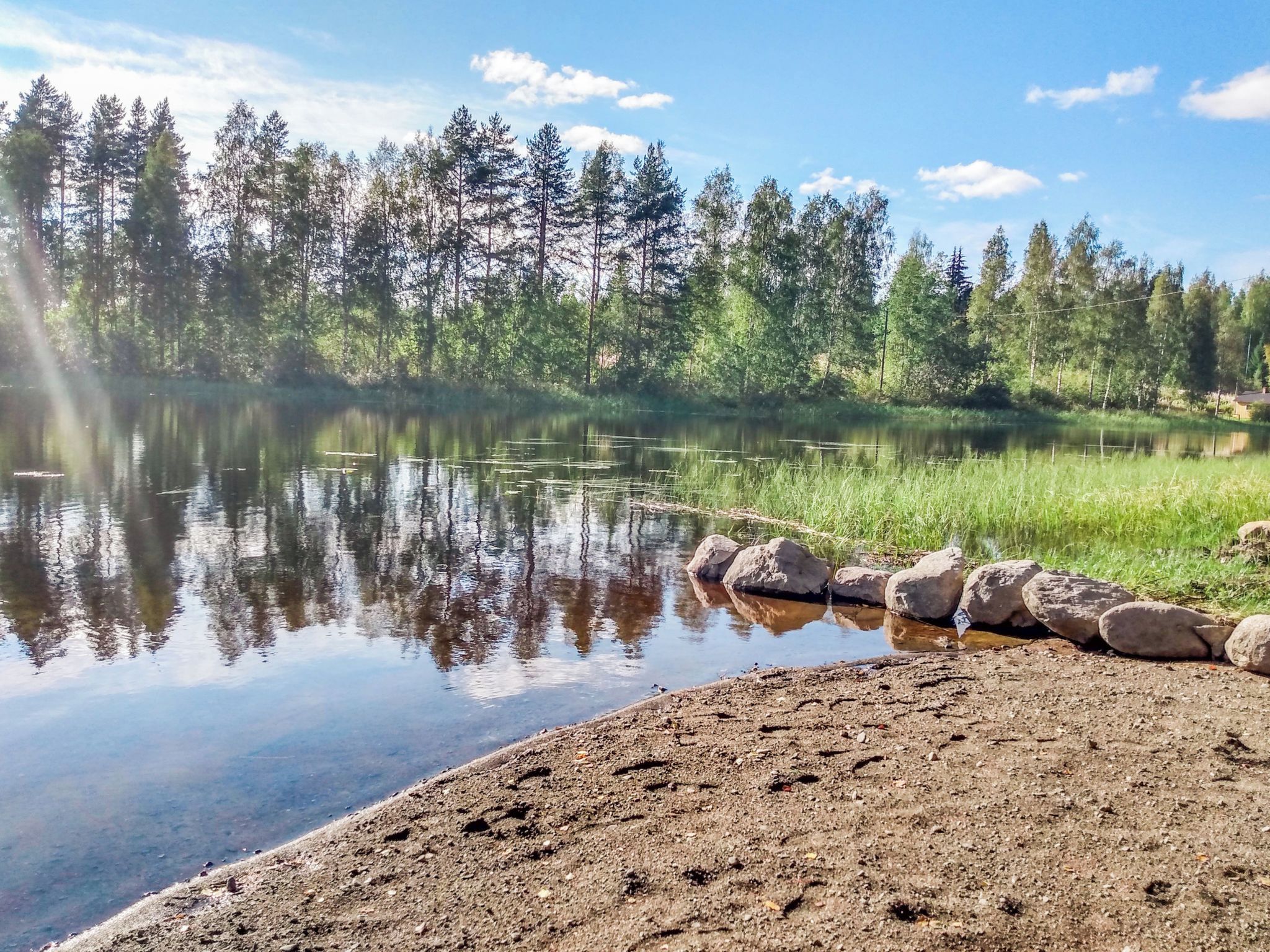 A natural landscape with a calm lake, surrounded by dense forest and a rocky shoreline.