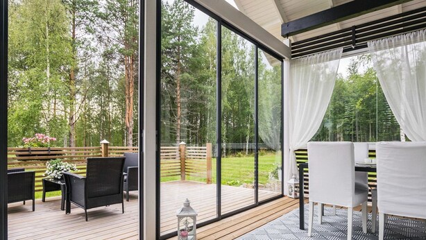 A covered outdoor area with a wooden deck, a table with chairs, and a view of a forested area. - Kaislaranta by Interhome (Suonenjoki)
