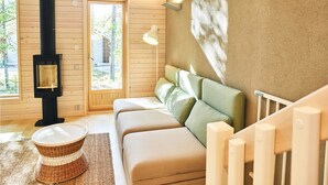 Een gezellige kamer met houten vloer, een bank, een geweven mand, een wandlamp en een raam met uitzicht op bomen.