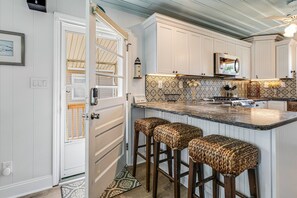 A kitchen with white cabinetry, a patterned backsplash, and a central island with bar stools. - Ocean Views from Front Deck, Steps to the Beach, Sleeps 8 (Oak Island)