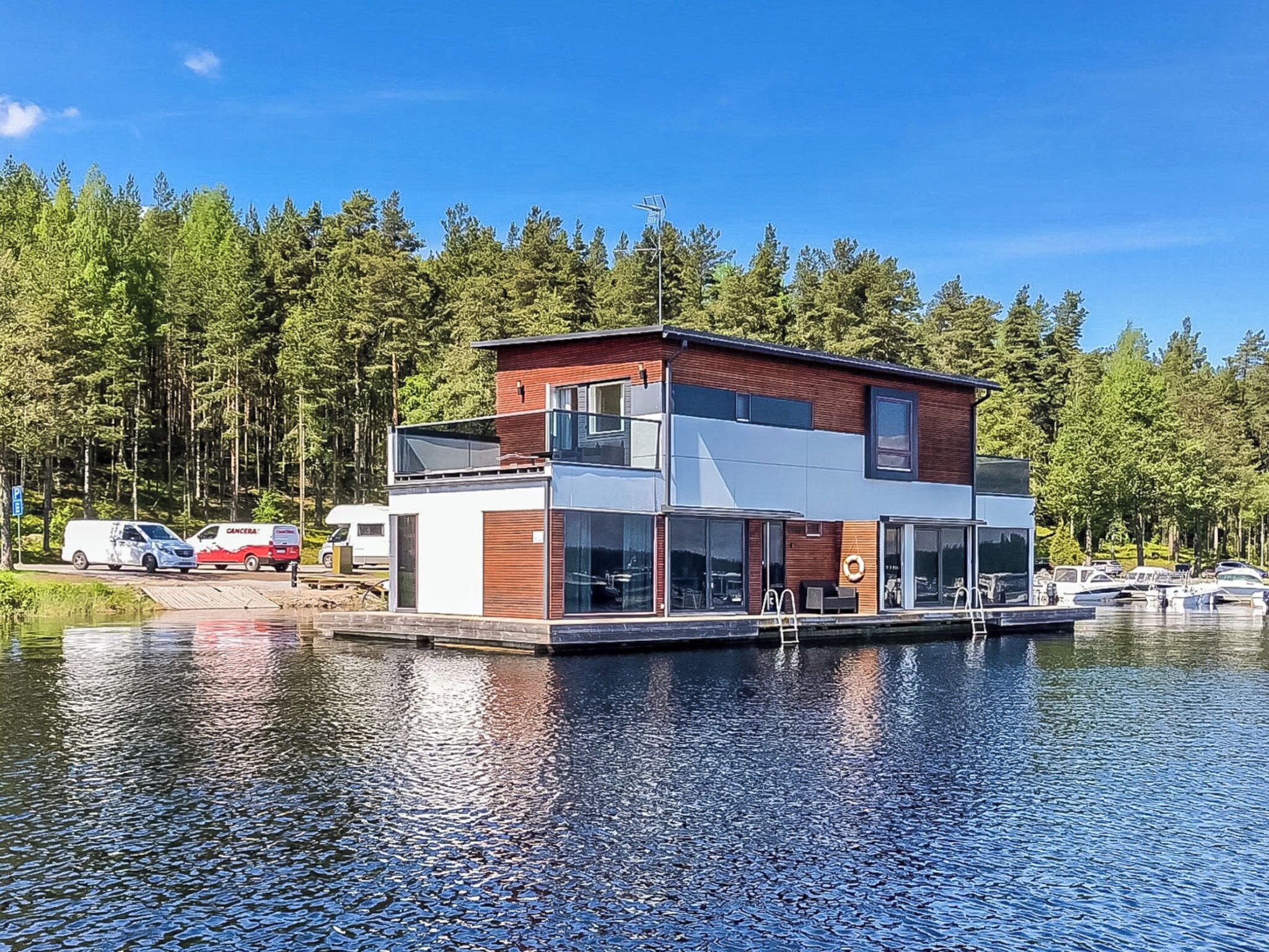 Une maison moderne à deux étages, dotée d’un quai, entourée d’une forêt et bordée par un plan d’eau.