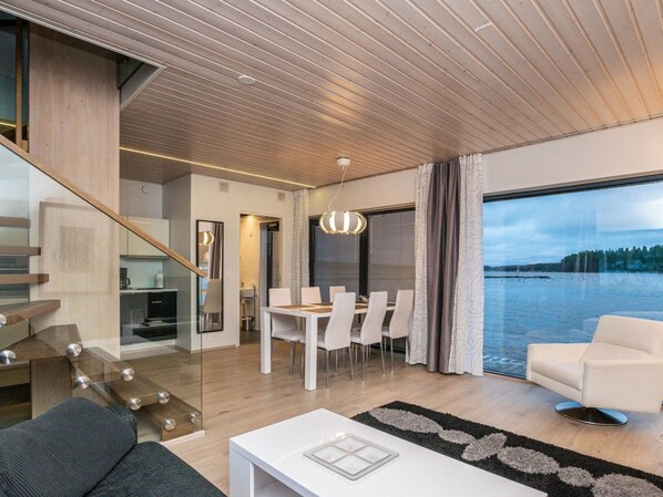 A modern living room with a dining area, a staircase, and a large window overlooking a body of water. - Villa joutseno by Interhome (Imatra)