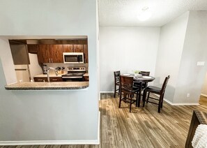 A compact kitchen with a microwave, sink, and wooden cabinets. Adjacent is a dining area with a table and chairs. - Spacious Poolside Oasis with Easy Access & Parking (Corpus Christi)