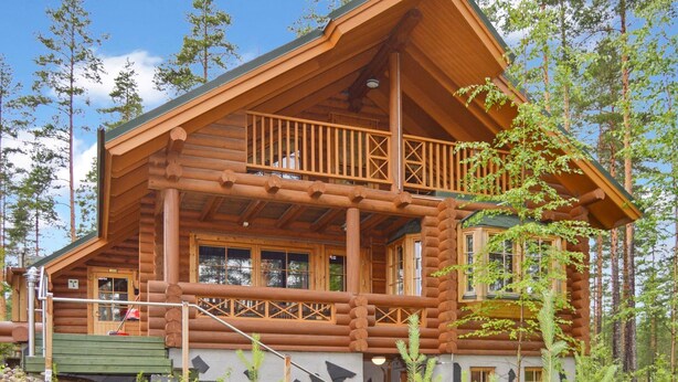 Une cabane en rondins dotée d’un balcon, entourée d’arbres.