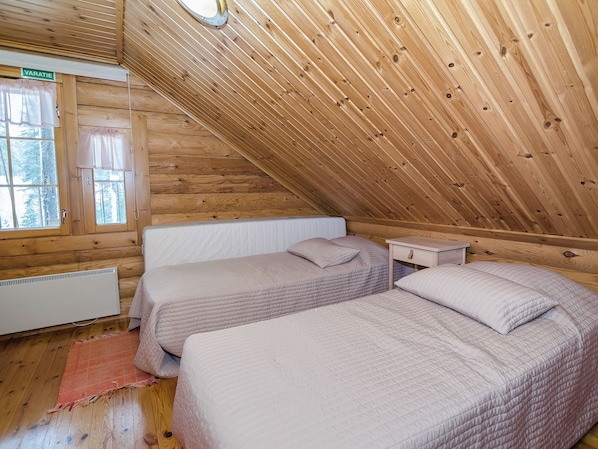 A wooden cabin with two beds, a window, and a radiator.