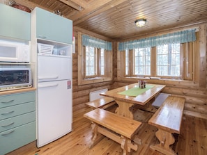 Een blokhutinterieur met een kitchenette, houten banken en grote ramen.