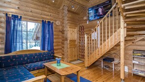 L’intérieur d’une cabane en rondins, avec un escalier en bois, un ensemble de canapés, un téléviseur et une bibliothèque.