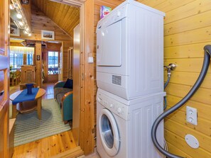 A compact room with a washing machine and a hose, wooden walls, a small seating area with a table and chairs, and a window with a view. - Villa käpytikka by Interhome (Liperi)