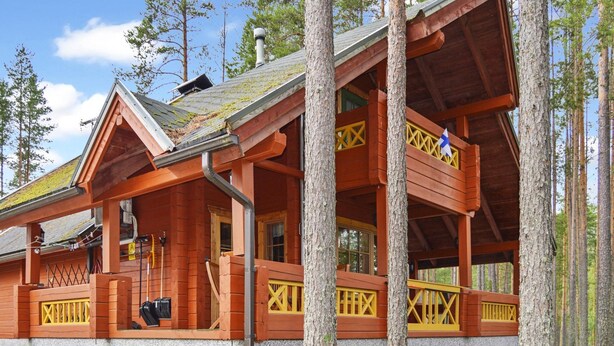 Une cabane avec une façade en bois, une véranda dotée de rampes jaunes et un banc vert à l’extérieur.