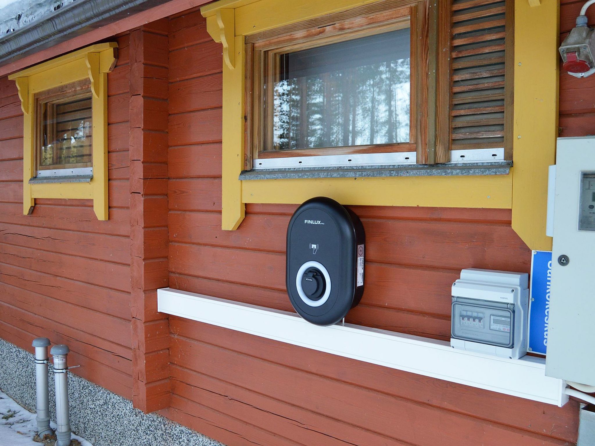 Une cabane en bois avec une fenêtre, un carillon et un coffret de raccordement électrique.