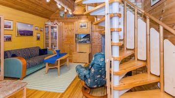 A cozy cabin interior with a spiral staircase, wooden walls, a sofa, a television, and a bookshelf.