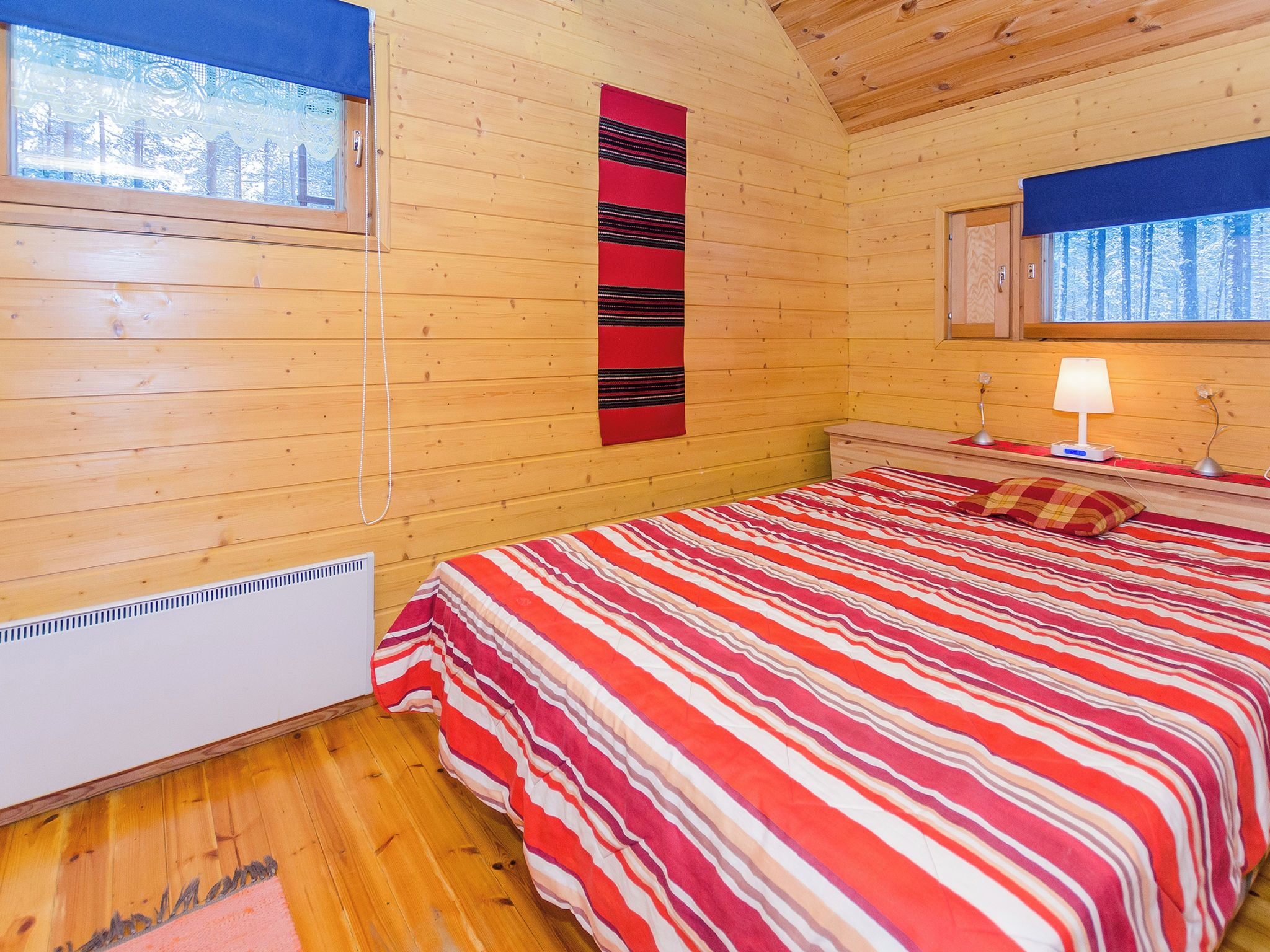 A wooden cabin room with a bed, a window, and a wall-mounted lamp.
