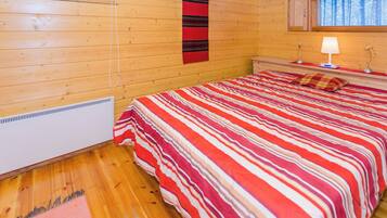 A wooden cabin room with a bed, a window, and a wall-mounted lamp.