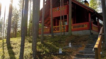 Une cabane en bois à l’extérieur rouge et aux accents jaunes, entourée d’une forêt, avec un escalier en pierre menant à l’entrée.