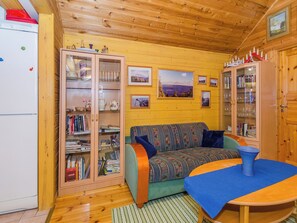 Interior acogedor de una cabaña con techo de madera, un sofá, una mesa y una estantería.