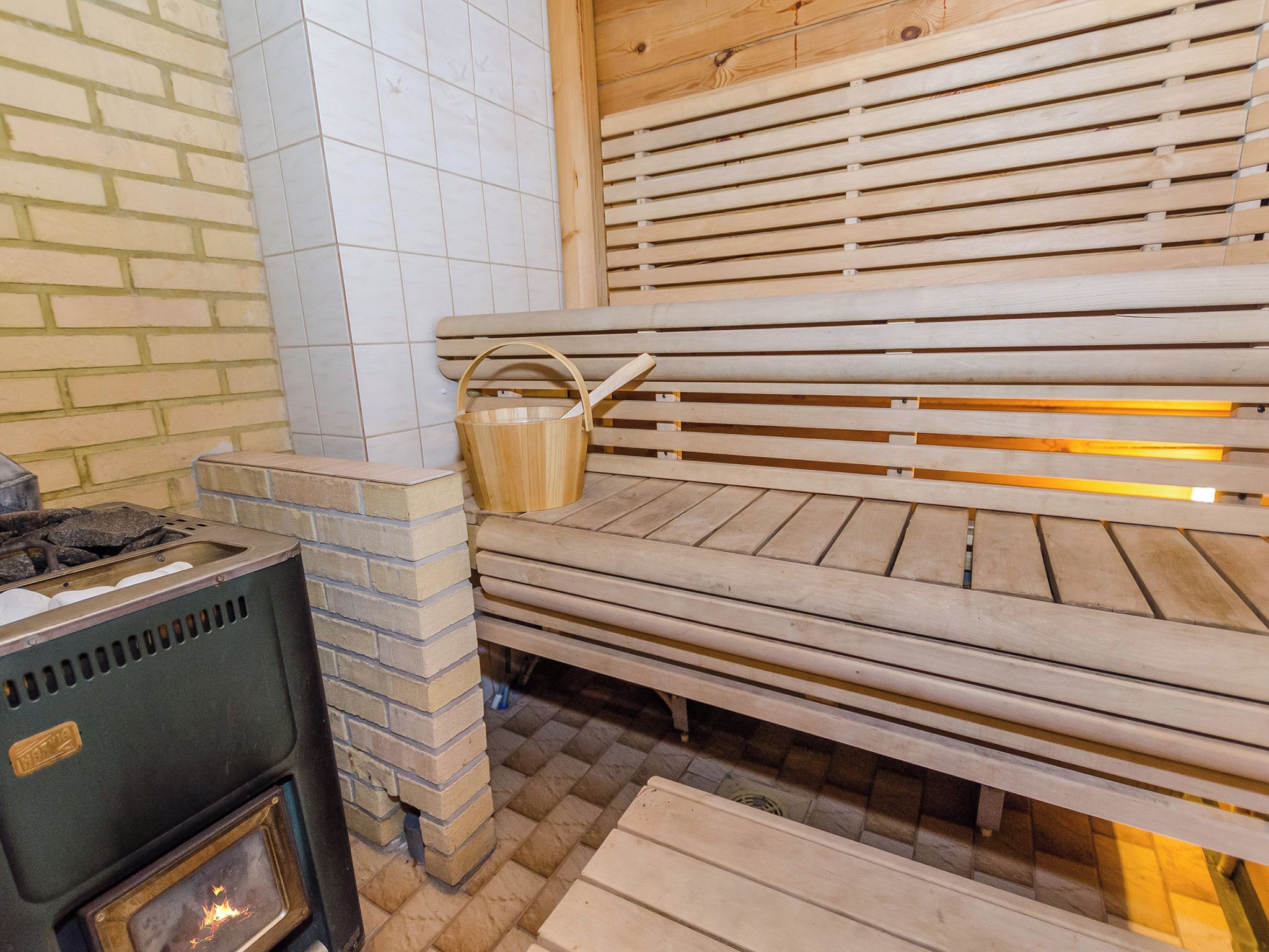 A sauna with wooden benches, a brick wall, and a tiled floor.