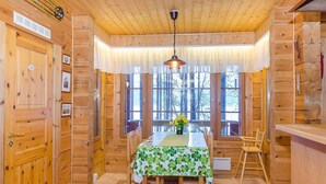 L’intérieur d’un chalet en bois comprend une table à manger, des chaises et une fenêtre donnant sur les arbres.