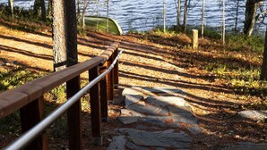 Un sentier de pierres bordé de rambardes en bois mène à un plan d’eau, qui est entouré d’arbres et auquel on accède par un canoë.